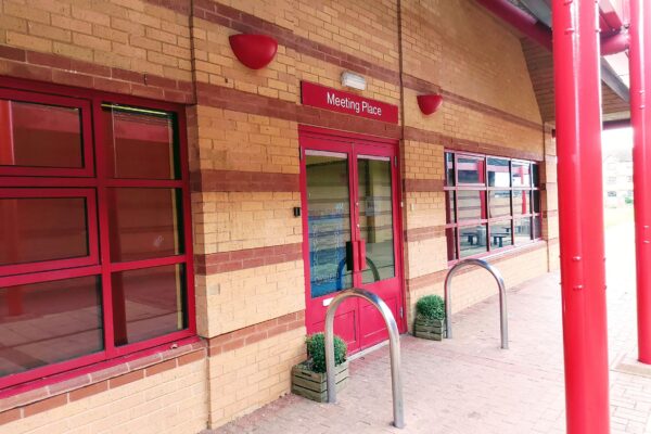 Front entrance, glass door with red surrounds and red sign with 'Meeting Place' overhead.