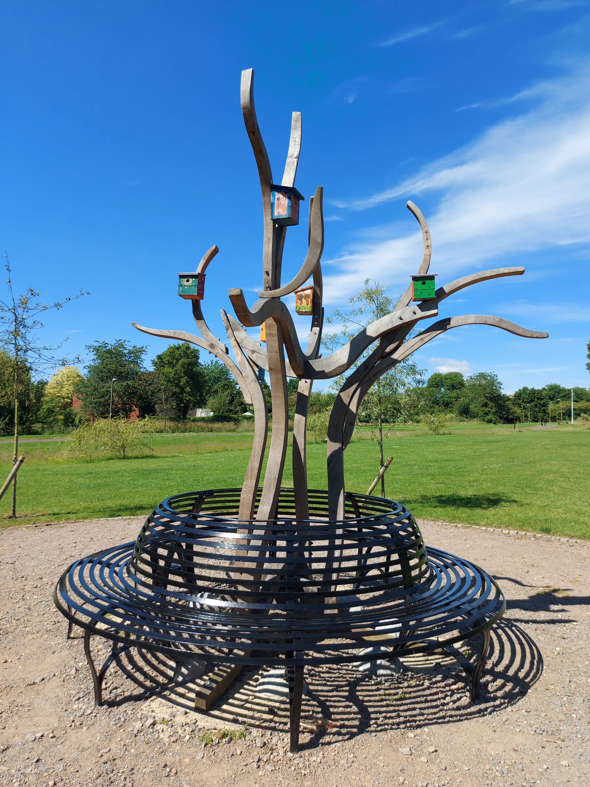 Stylistic wood sculpture of a tree surrounded by a black iron bench