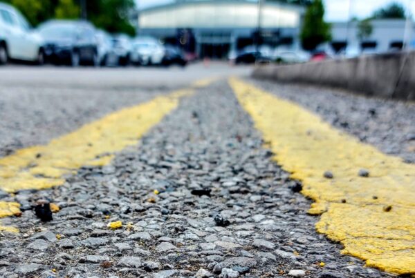 Close-up picture of double yellow lines on a road lined with cars on the opposite side