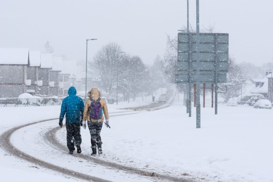 Two people walking on a road covered in snow.