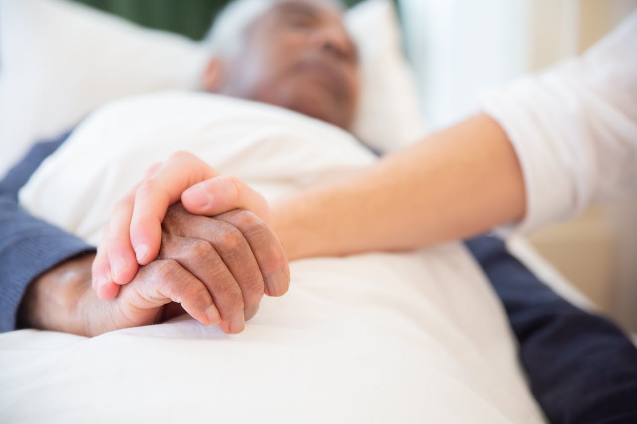 Young person holding the hand of an older person who is lying in bed