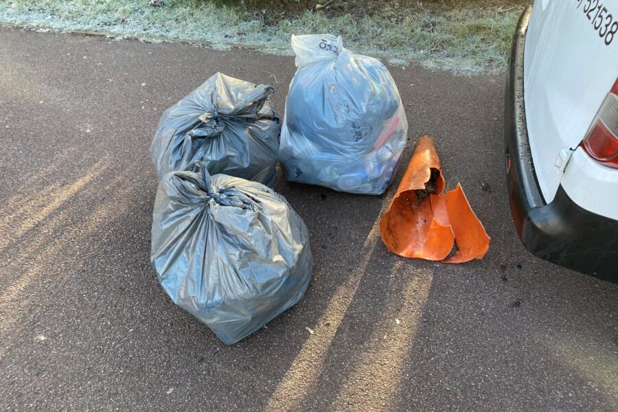 Three full bin bags and a broken traffic cone next to the rear bumper of a white van